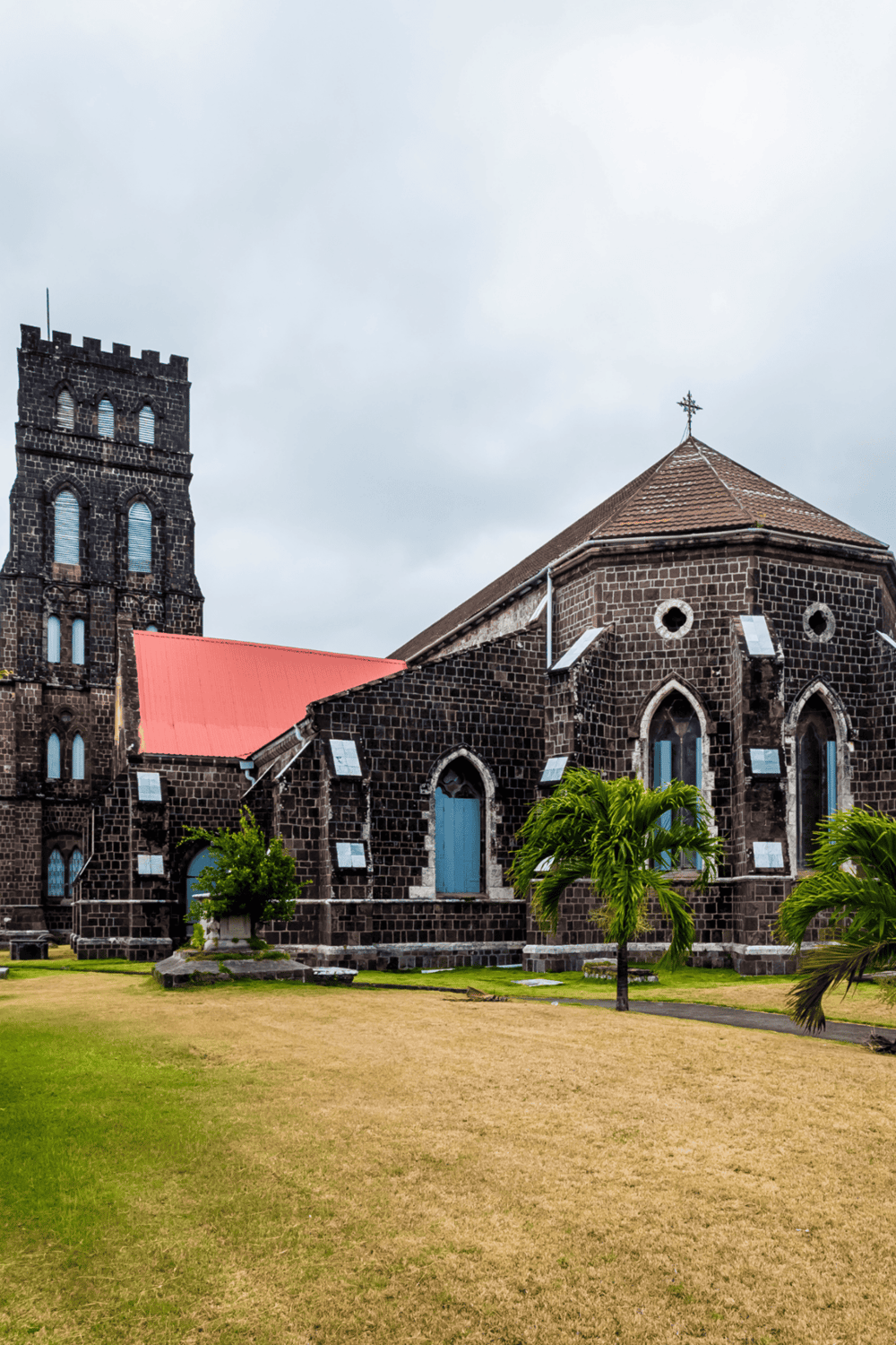 Historic stone church in a tropical setting with palm trees and cloudy sky.