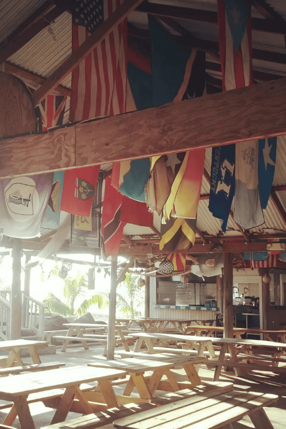Colorful flags hanging in a rustic outdoor dining area with wooden picnic tables.