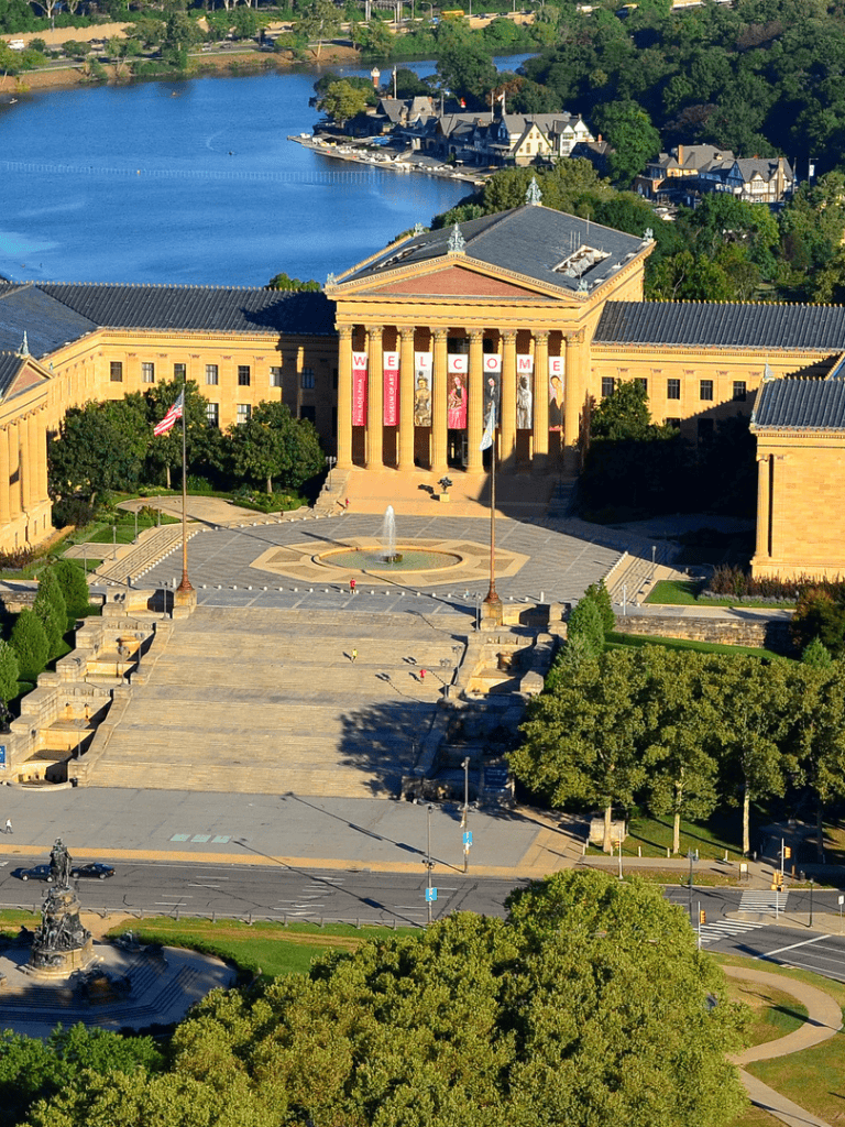 Historic government building with impressive columns and welcoming banners, surrounded by lush greenery and scenic water views.