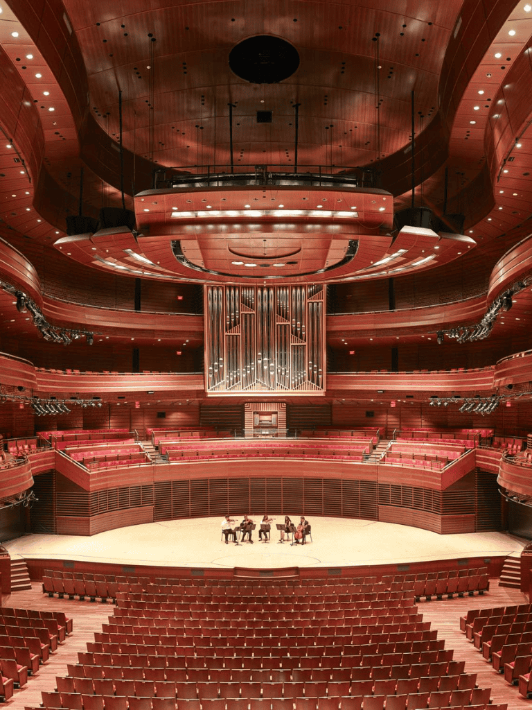 Orchestra rehearsal inside a modern concert hall with wooden interiors and stage lighting.