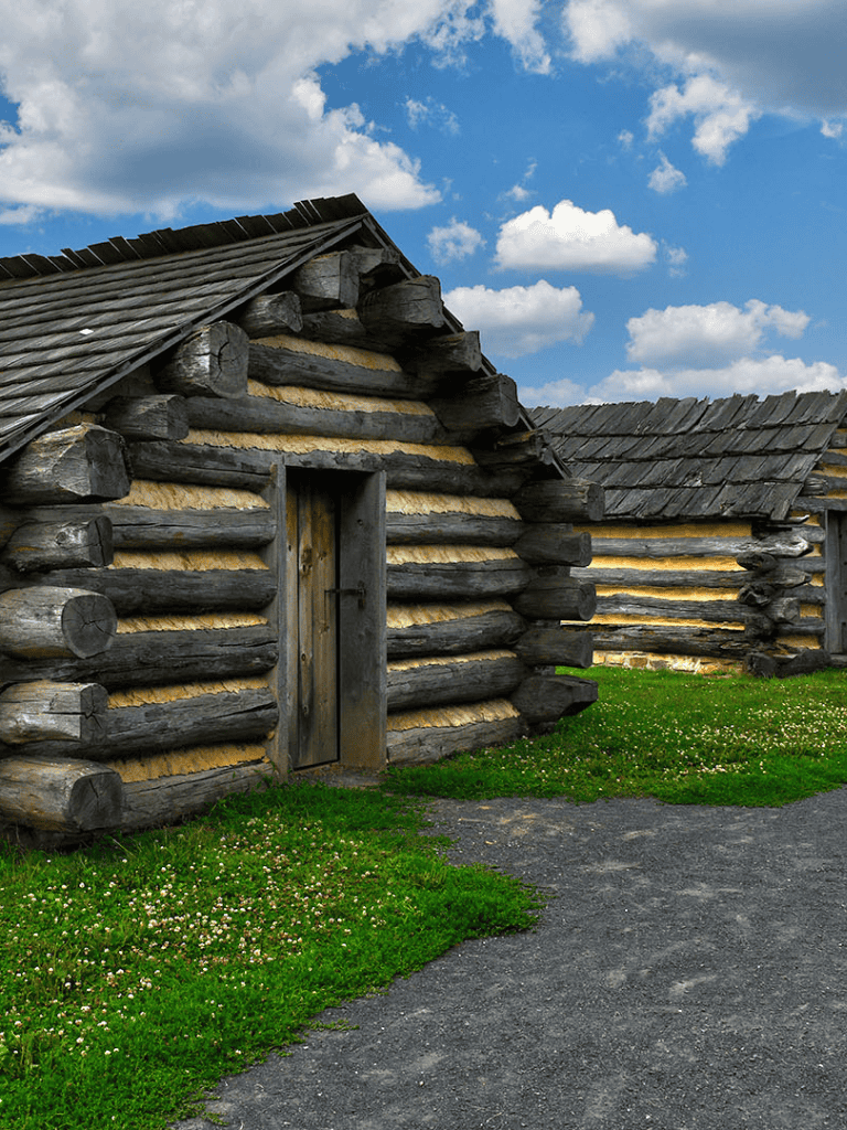 Weathered log cabins in a scenic rural setting with blue sky and clouds, perfect for outdoor adventure and history exploration.