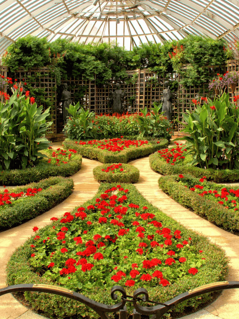 Colorful flower garden inside a glass conservatory with greenery and sculptures.