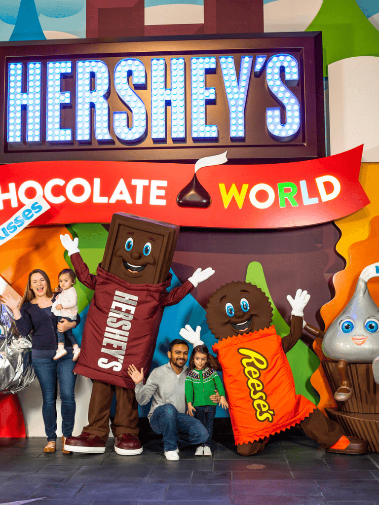Bright Hershey's chocolate theme park entrance with mascots and visitors, colorful signage and cheerful atmosphere.