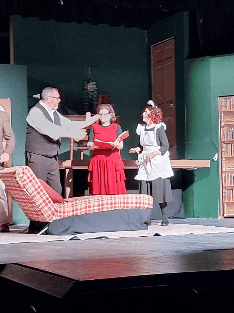 1. Stage play scene with actors in vintage costumes, theater set background, and a plaid sofa.