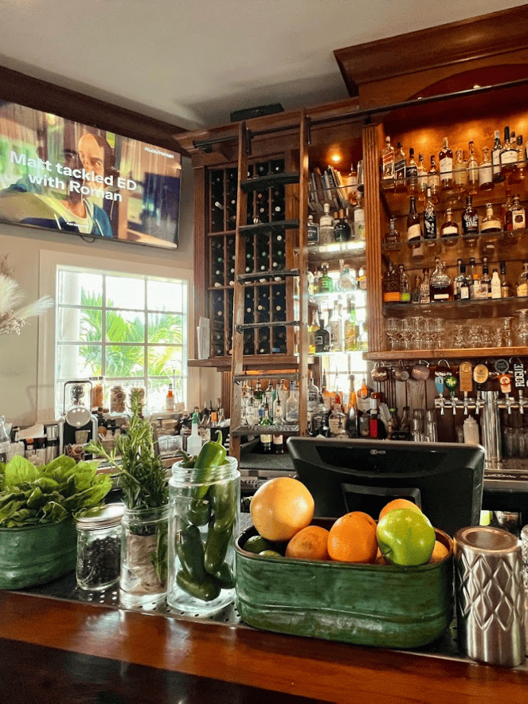 Fresh herbs and produce display at QuestForDirections bar; cozy ambiance, extensive liquor selection, and TV in background.
