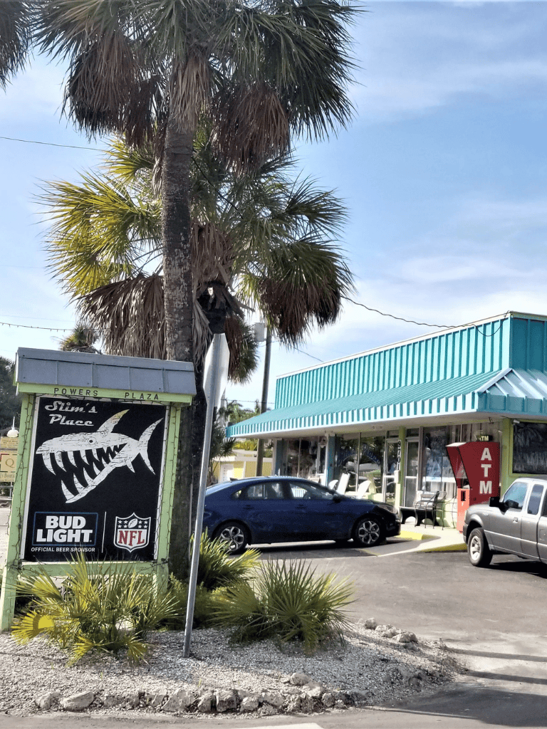Palm trees and a local business storefront with parking in sunny weather.