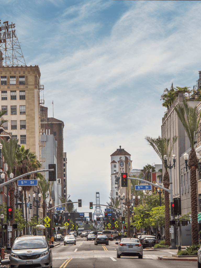 Downtown San Diego street view with palm trees, traffic signals, and the Coronado Bridge in the background.