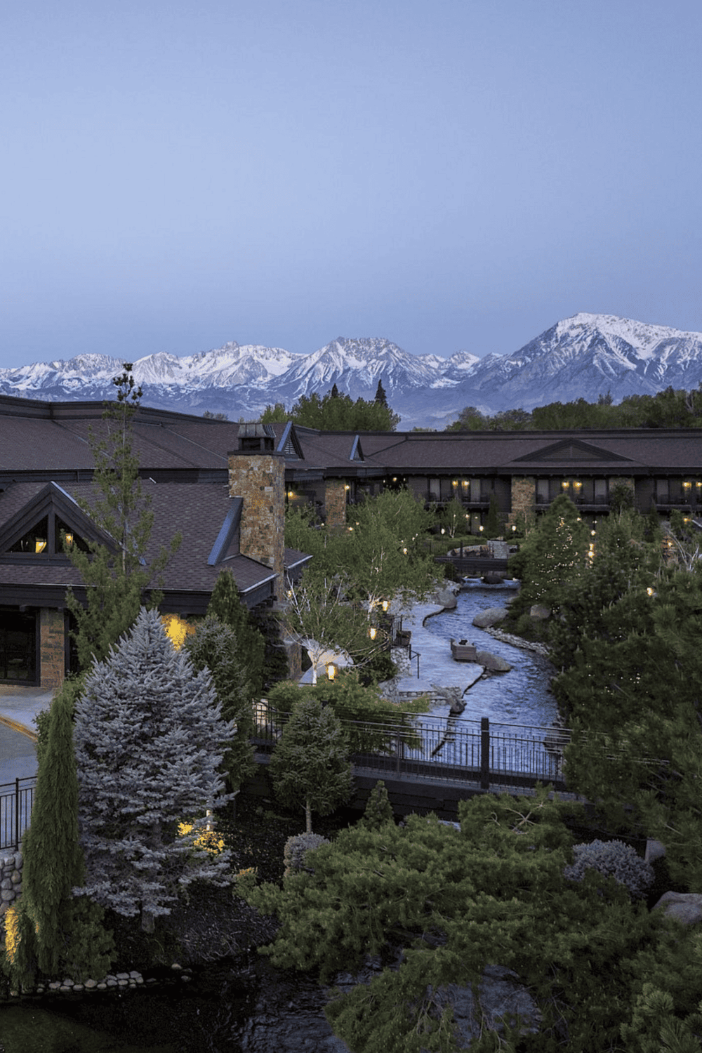 Serene mountain resort with snowy peaks, lush greenery, and tranquil river scenery.