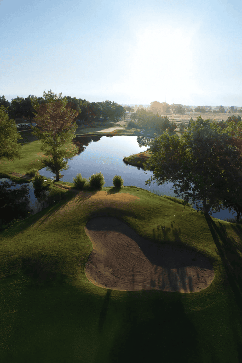 1. Golf course with water hazard and sand trap during sunset, scenic outdoor sports activity.