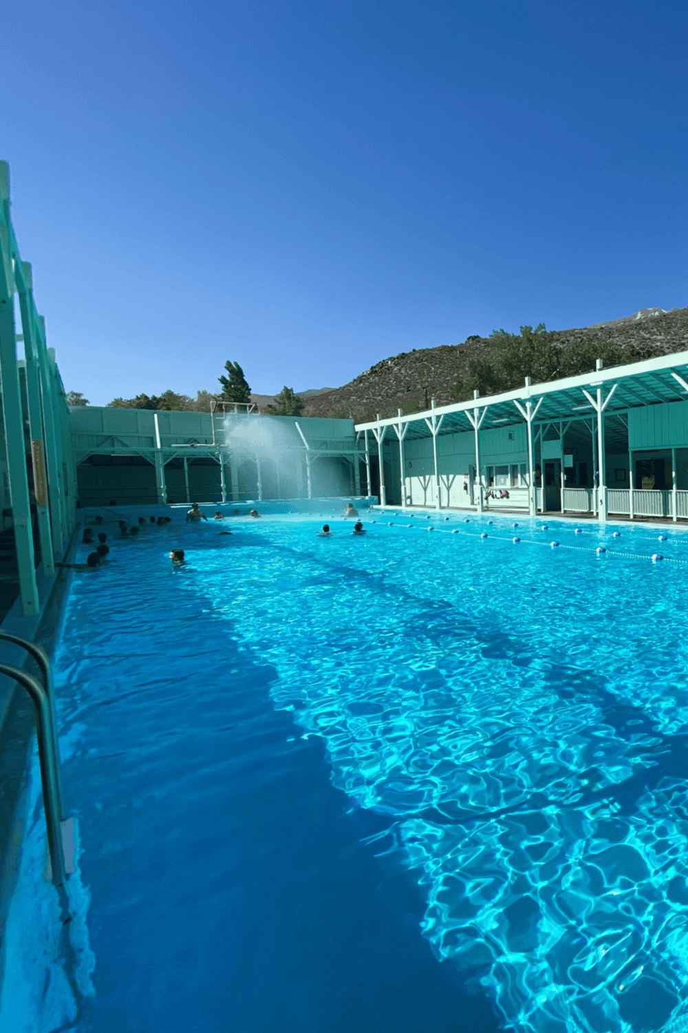 Outdoor swimming pool at Quest for Directions with people enjoying the water and mountain scenery in the background.