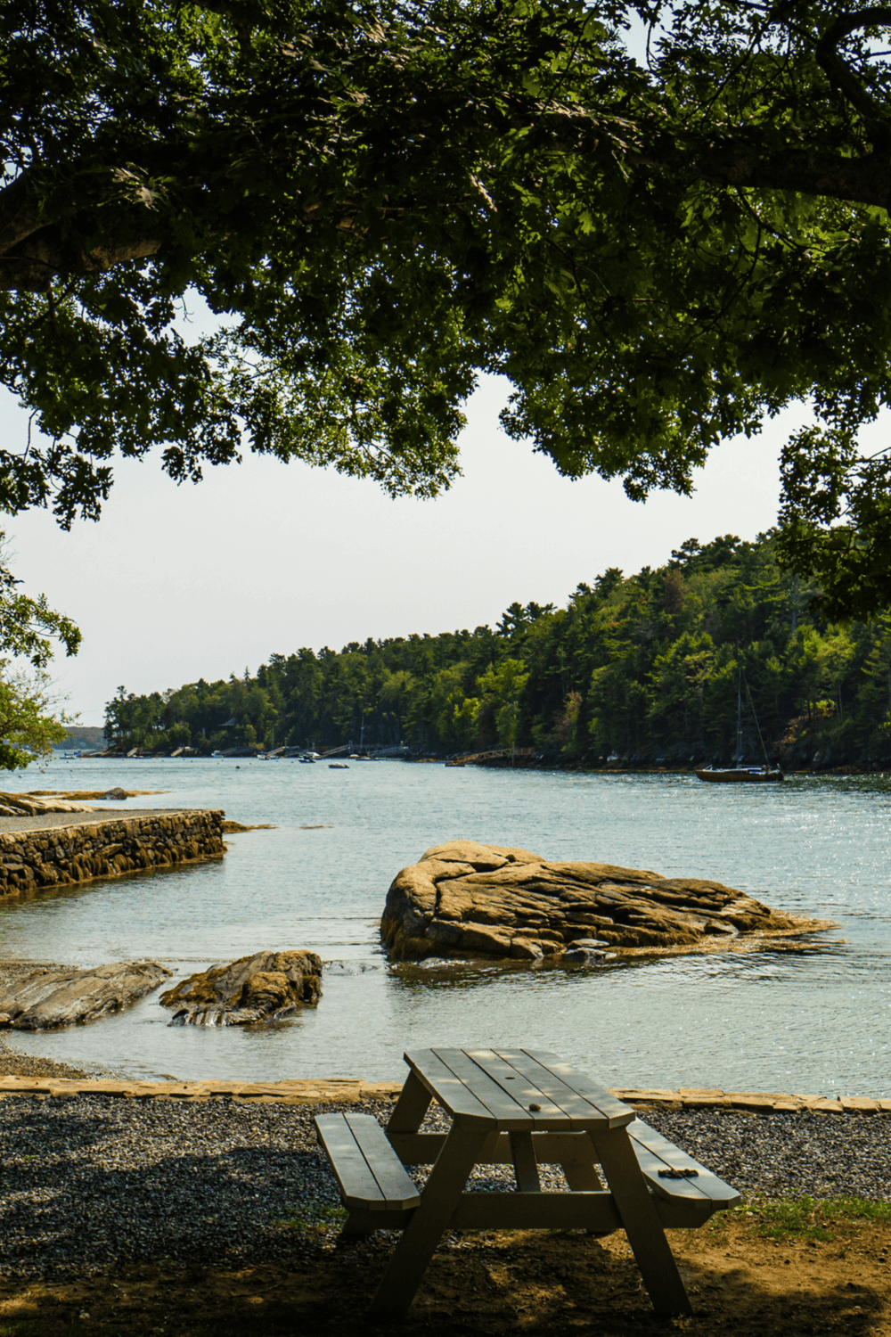 Scenic lakeside view with trees, rocks, and boats, perfect for outdoor adventure and relaxation.