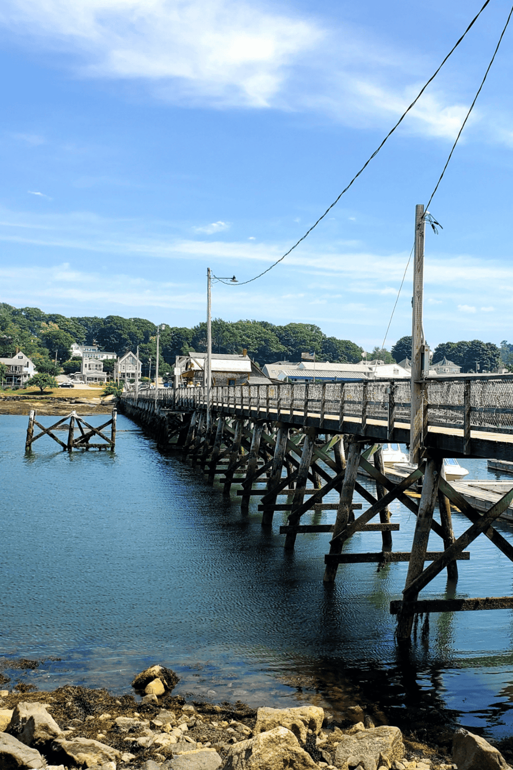 Wooden pier extending over water in a coastal village with houses and lush greenery in the background.