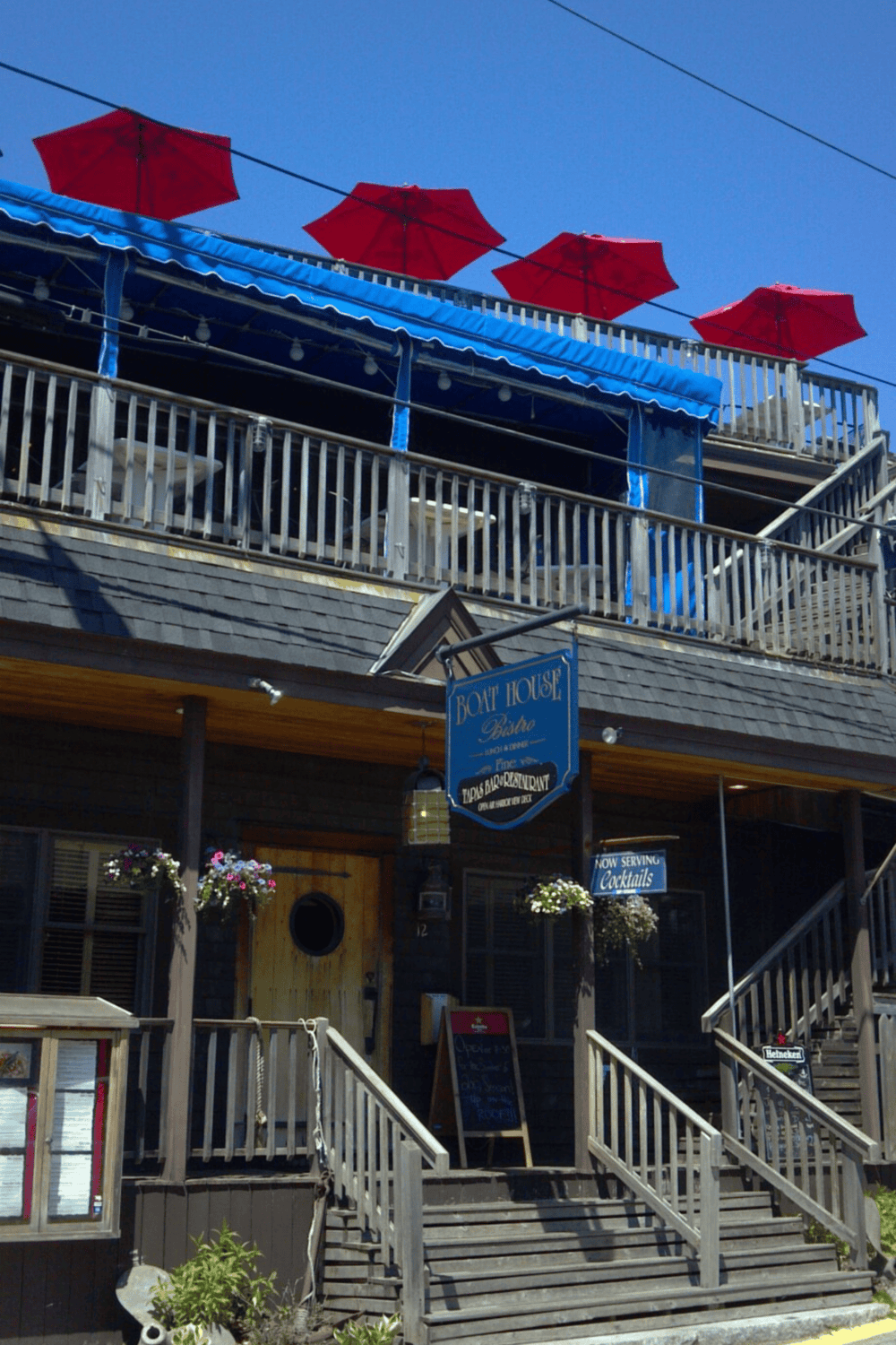 Alto text: Coastal boat house restaurant with outdoor seating and red umbrellas.