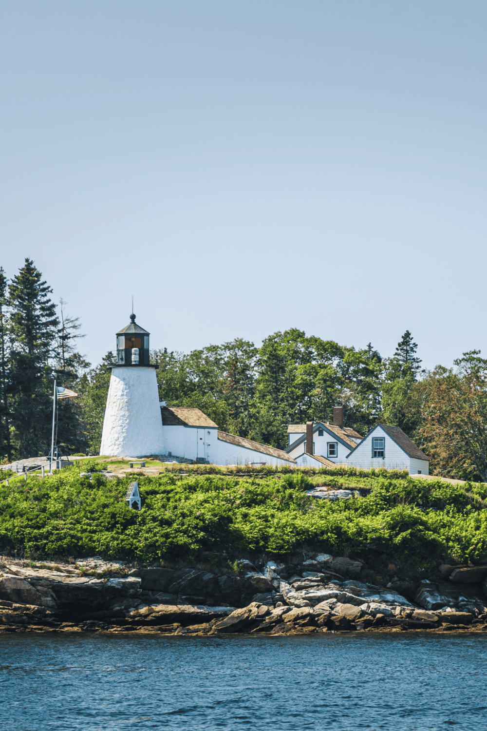 Seaside lighthouse and lighthouse keeper's house on rocky coastline with water in foreground.