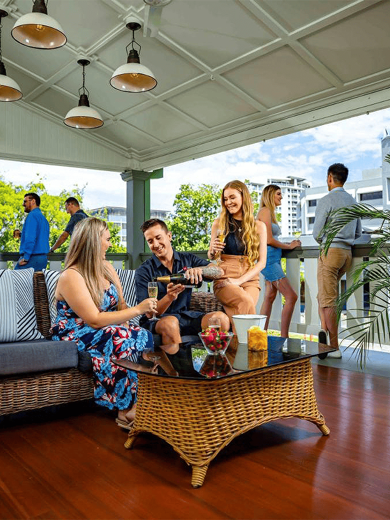 Elegant outdoor social gathering on a balcony with guests enjoying wine and conversation in a modern urban setting.