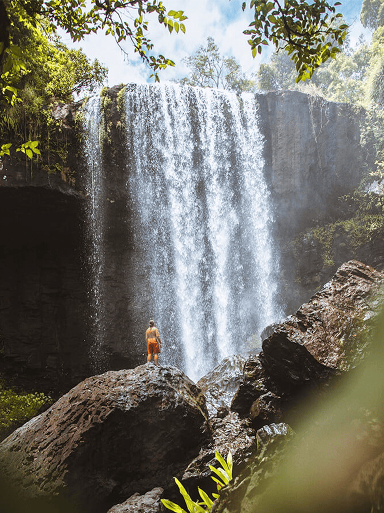 Waterfall in lush forest with person standing on rocks, nature adventure destination.