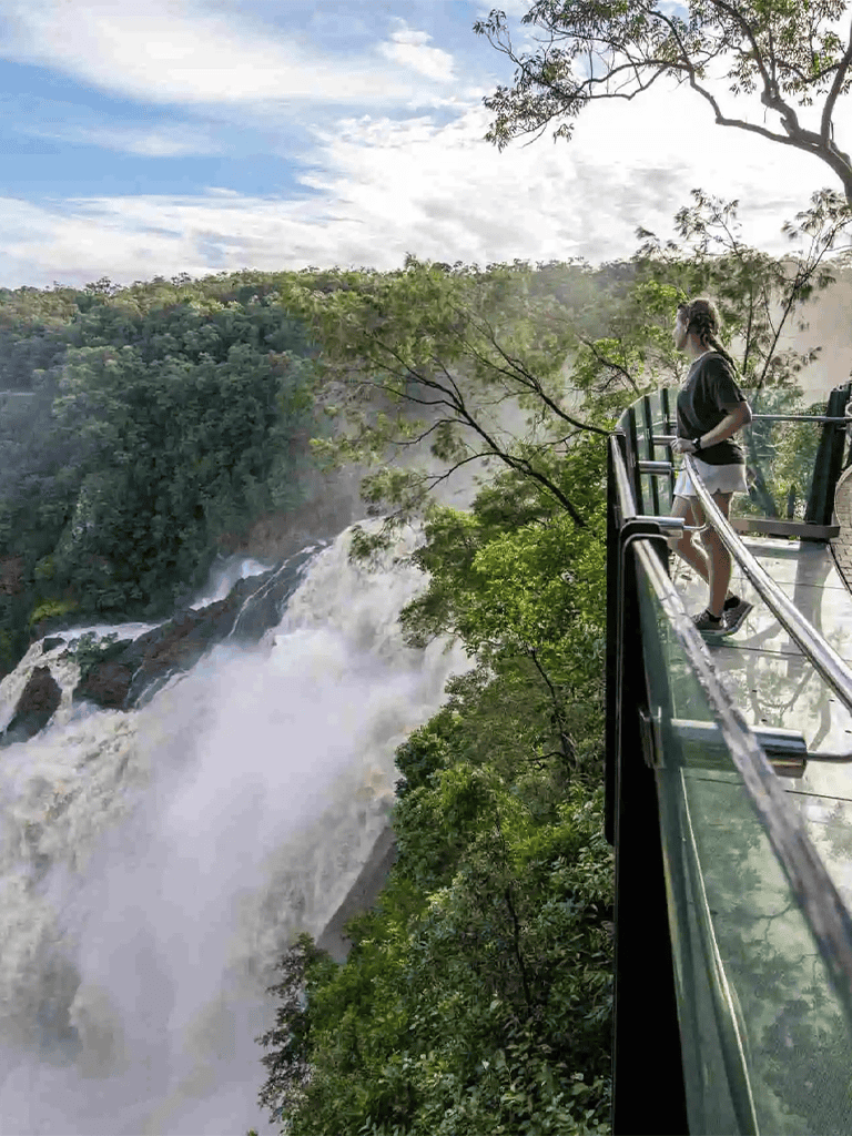Vivid waterfall view from a glass observation deck in lush green rainforest environment.