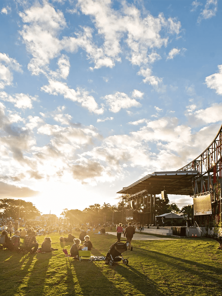 Colorful outdoor concert with audience enjoying sunset at park, diverse group, stage setup, family-friendly event.
