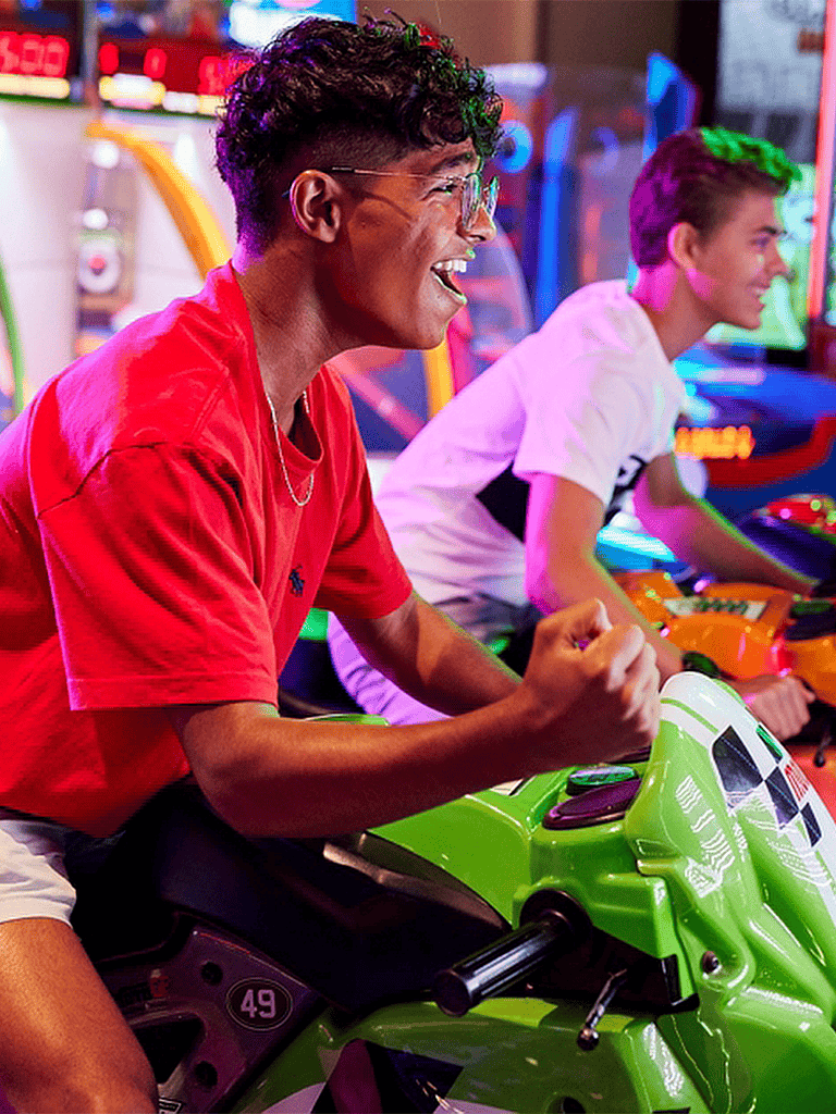 Vibrant arcade game room with smiling teenagers enjoying racing simulator rides for entertainment.