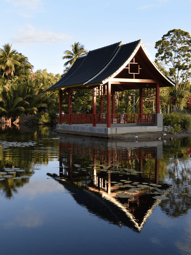 Serene Japanese-style garden pavilion over water with lush tropical trees.