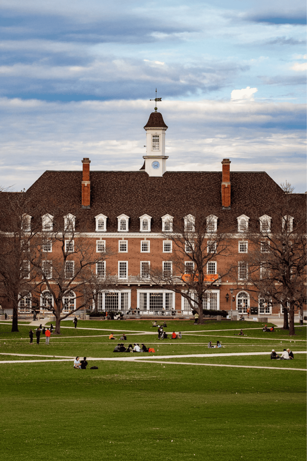 1. Historic brick building with clock tower and park scene in front, fall trees, blue sky.