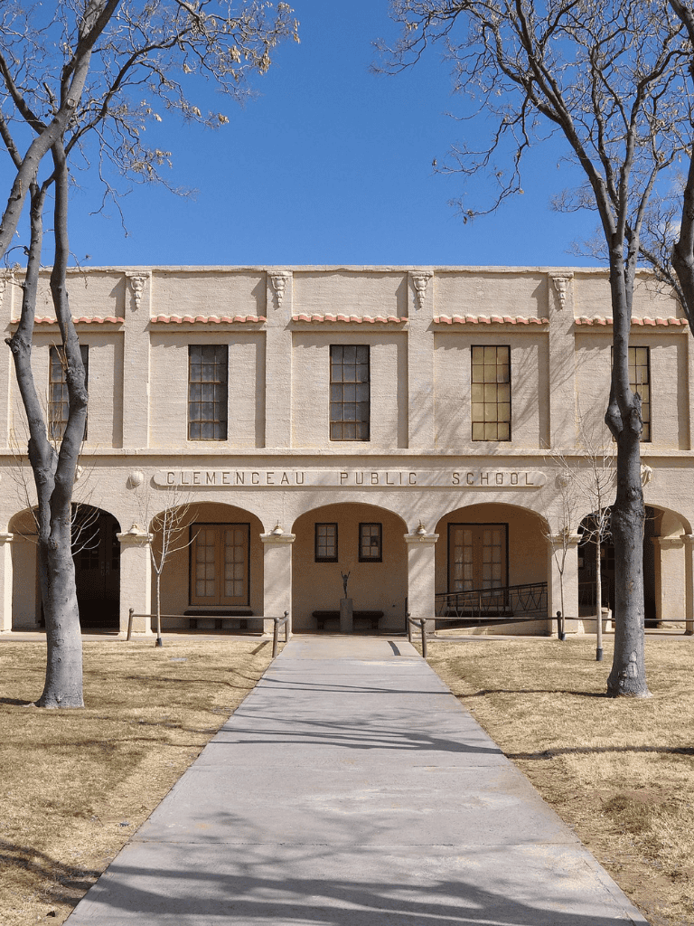 Historic Clemenceau Public School building with pathway and leafless trees under clear blue sky.