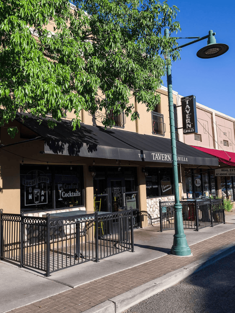 Outdoor view of The Tavern Grille restaurant with black awning and street lamp, located in a small shopping district.