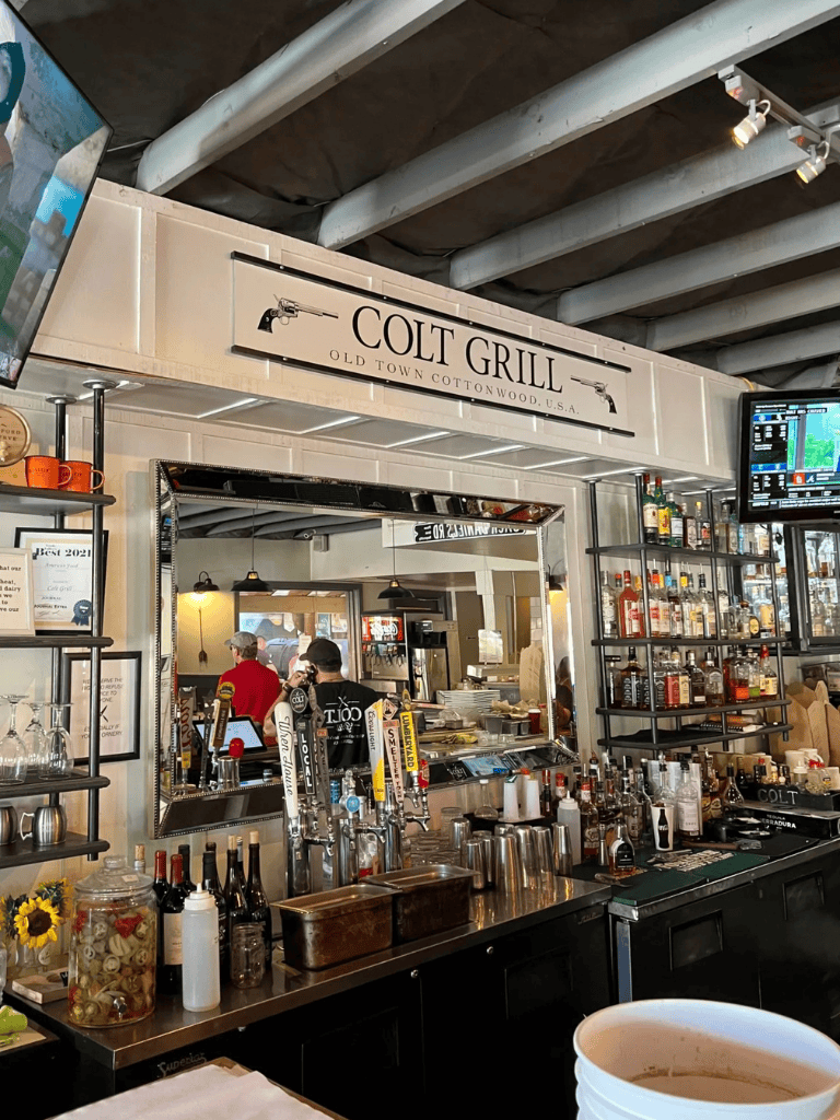 Rustic bar at Colt Grill with craft beer taps and liquor bottles, industrial ceiling and lively atmosphere.