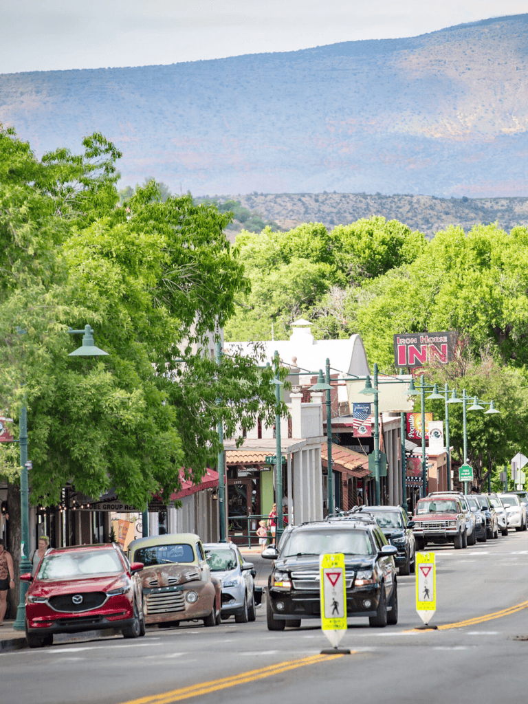 Charming small-town street with shops, restaurants, and parked cars, scenic mountain backdrop, perfect for travel planning.