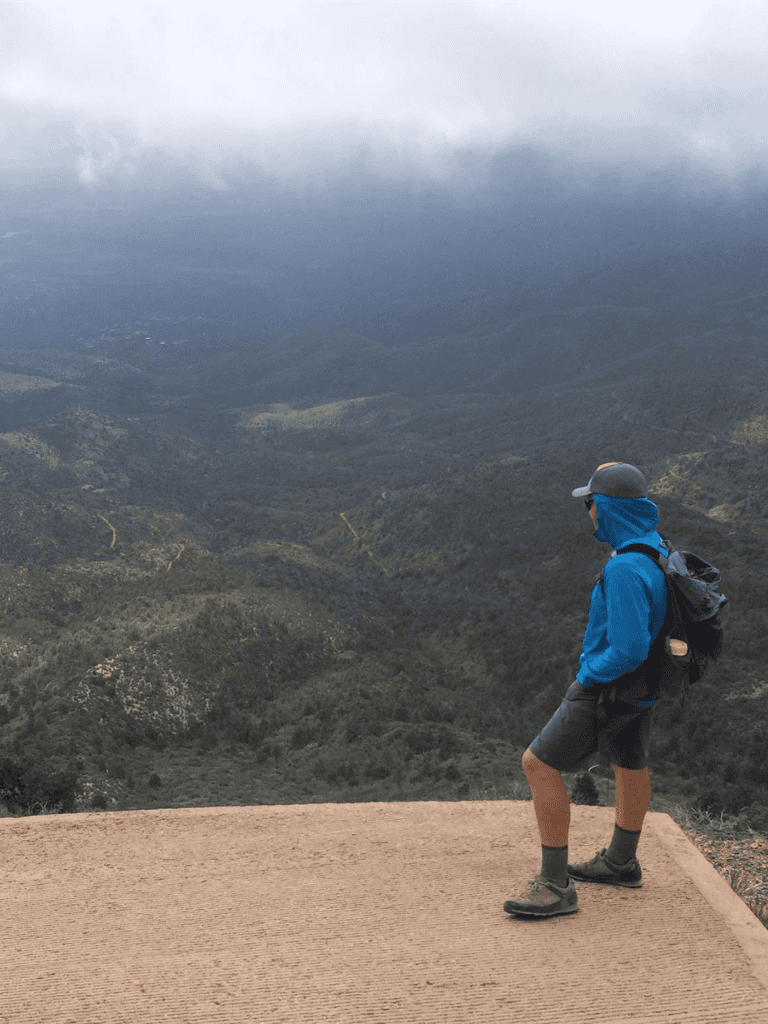 Bright blue hiking jacket with backpack on a mountain overlook in foggy landscape.