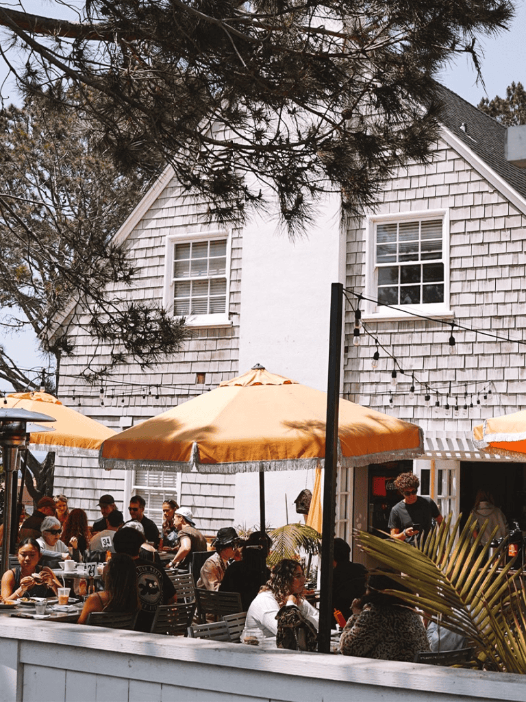 Outdoor dining at Quest For Directions restaurant on a sunny day with umbrellas and a lively crowd.