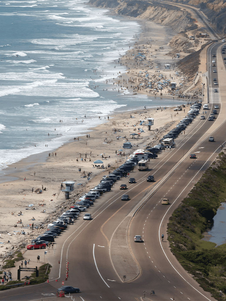 Beach parking lot along scenic coastal highway during busy summer day, crowded beach access.