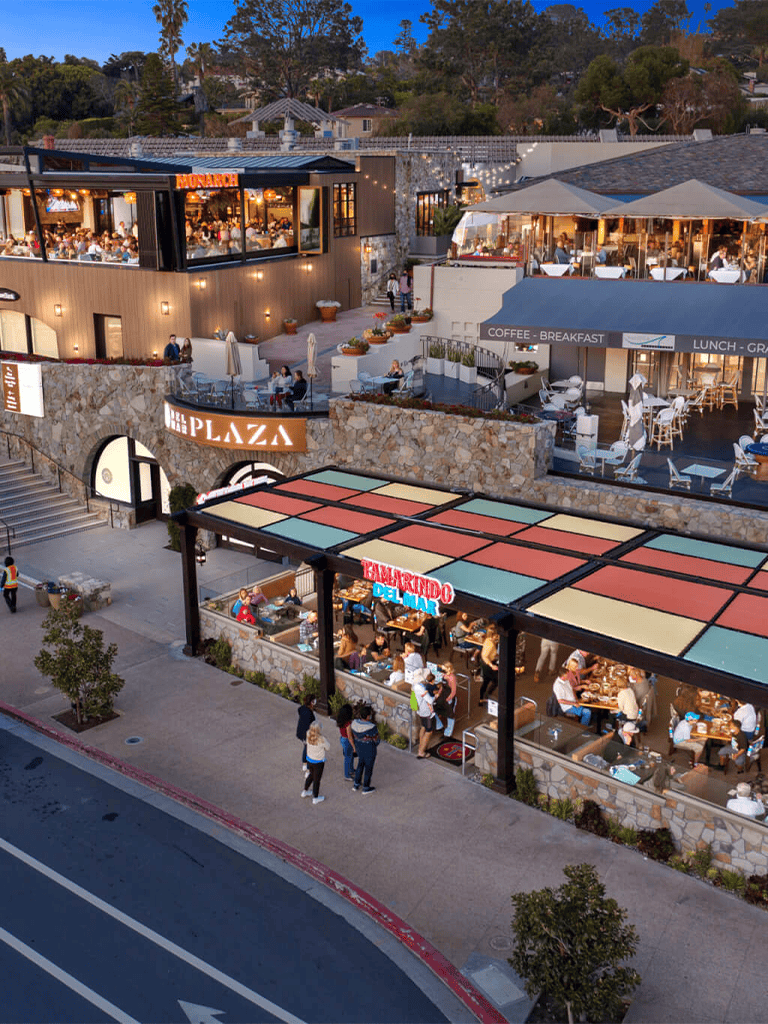 Vibrant outdoor dining and shopping plaza with restaurants and cafes at dusk.