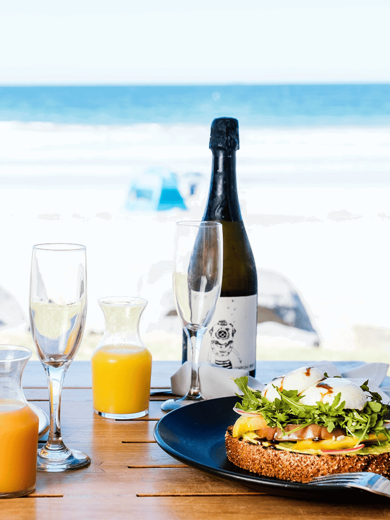 Refresh your day with seaside brunch featuring champagne, fresh juice, and poached eggs on toast by the ocean.