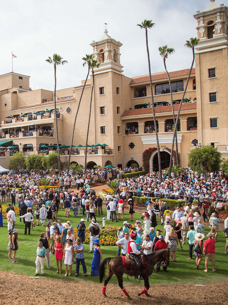 Vibrant horse race event at a historic hotel with a lively crowd and scenic palm trees.