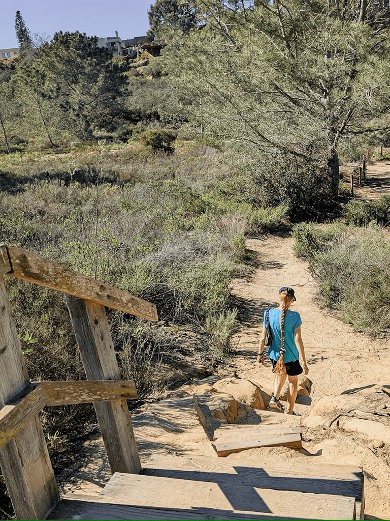 Secluded hiking trail through nature with woman walking on rocky path.