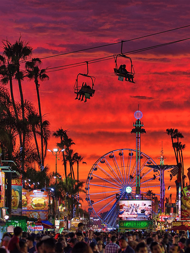 Vivid sunset at a lively carnival with Ferris wheel and amusement rides in the evening twilight.