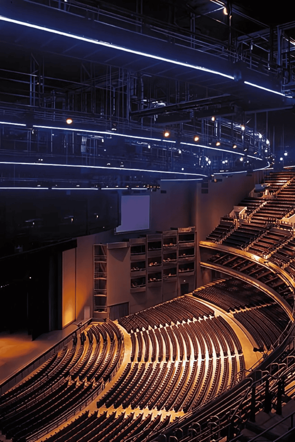 Blue stage lighting illuminates a modern auditorium with tiered seating and high-tech equipment.