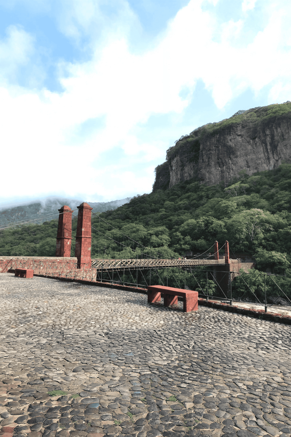 Suspension bridge over lush green mountains with rocky cliffs in the background, scenic outdoor landscape.