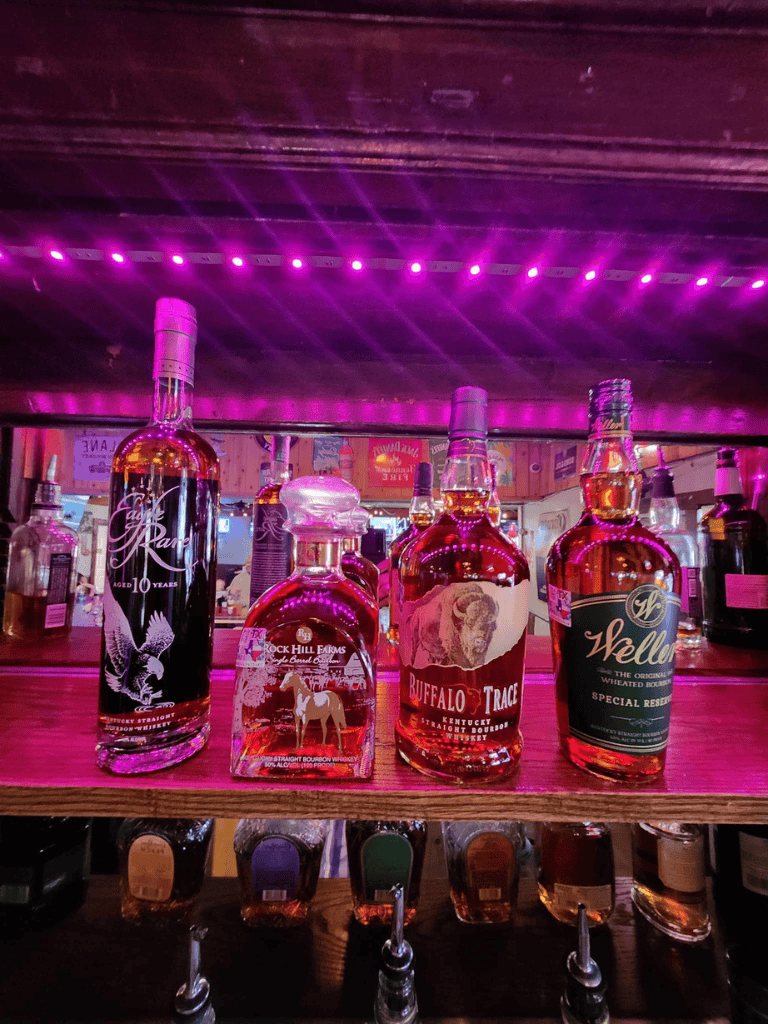 A bottle of bourbon whiskey on a bar shelf under pink neon lights.
