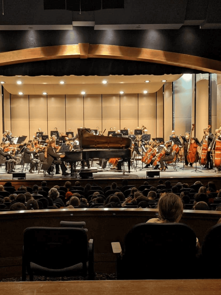 Elegant symphony orchestra performing live at concert hall with grand piano and string instruments, audience enjoying classical music event.