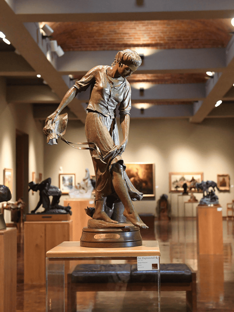 Bronze sculpture of a woman walking in art gallery, artwork display, museum sculpture, modern art piece, art exhibit, gallery artwork.