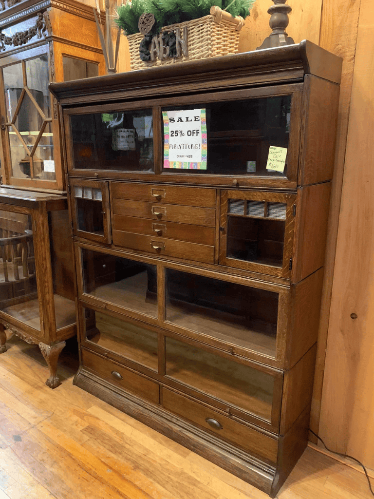 Antique wooden cabinet with glass doors and sale sign, perfect for vintage furniture enthusiasts.