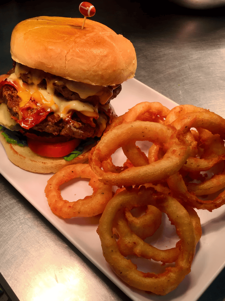 Juicy cheeseburger with crispy onion rings on a white plate, perfect for fast food lovers.