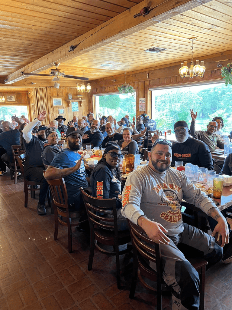 Joyful group of friends and family celebrating at a restaurant with large windows, wooden interior, and lively atmosphere.