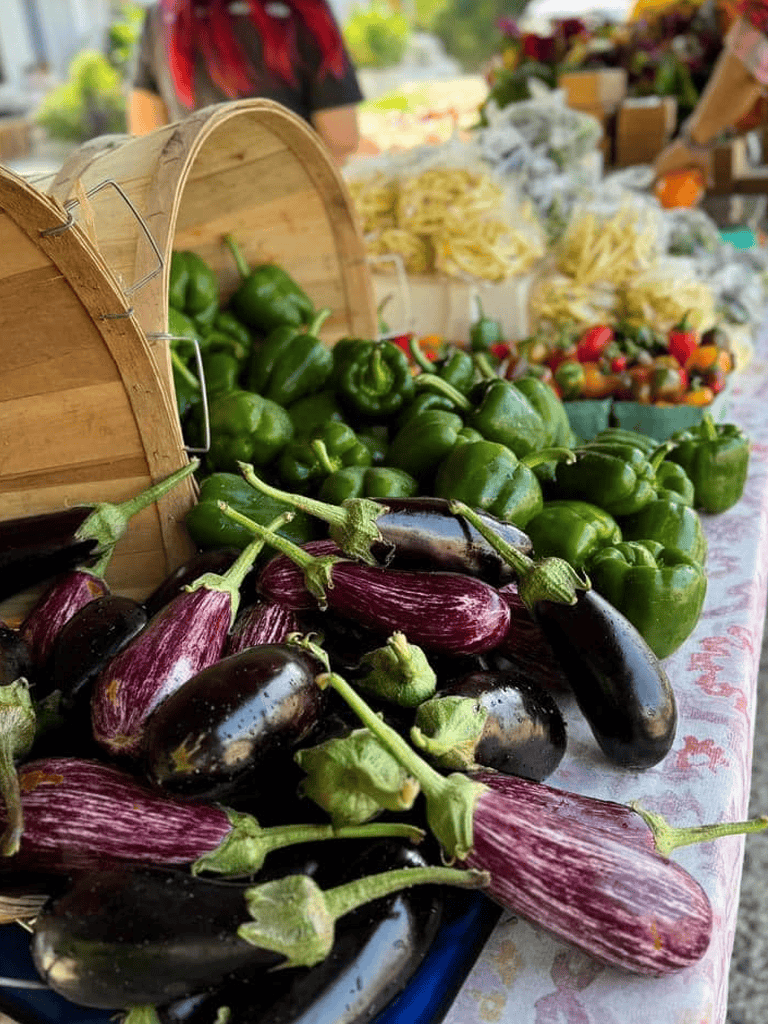Fresh green bell peppers and eggplants at a farmers market stand.