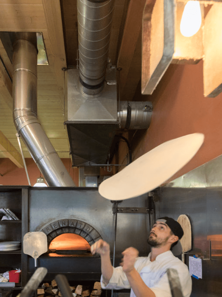 High-temperature pizza oven with a chef preparing dough, warm glow, professional kitchen setting.