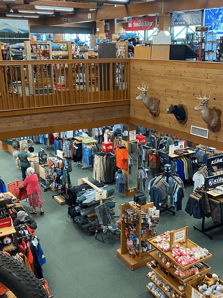 Comfortable indoor retail shopping store with outdoor gear and apparel, featuring mounted deer heads and a cozy rustic ambiance.