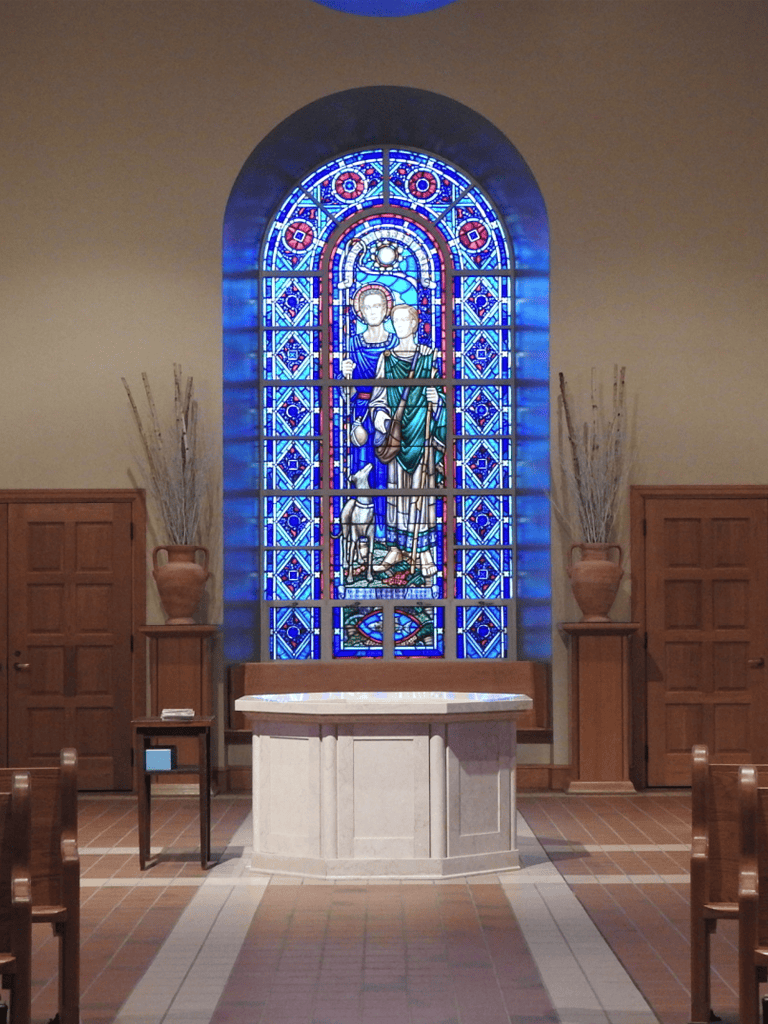 Vibrant stained glass window in church interior with altar and wooden decor, emphasizing spiritual ambiance.