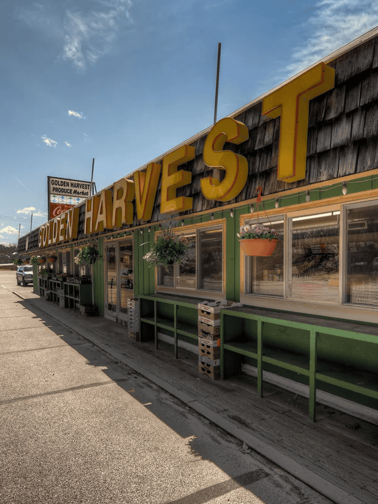 Golden Harvest Produce Market exterior with colorful signage and hanging flower baskets in a small town setting.